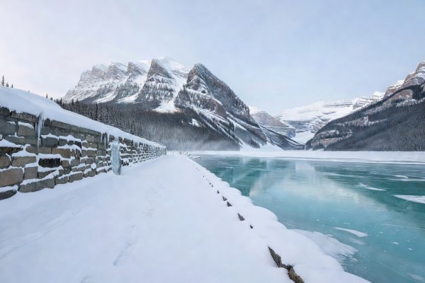 Snowy promenade and stone retaining wall overlooking frozen turquoise-tinted Lake Louise and Victoria Glacier