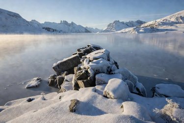 Rocky promontory covered in frost overlooking frozen Lake Sils in the Engadin valley